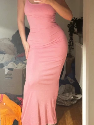Rosa långklän  - Säljer en rosa långklänning med smala axelband och figurnära passform. Klänningen är ärmlös och har en enkel, stilren design som framhäver siluetten. Perfekt för dig som gillar en feminin och trendig look.