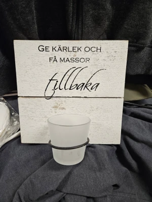 Väggskylt med text och ljushållare - Dekorativ väggskylt i vitt trä med svart text 'Ge kärlek och få massor tillbaka'. Skylten har en frostad glashållare för värmeljus och metallfästen på baksidan för enkel upphängning. Perfekt som inredningsdetalj i hemmet.