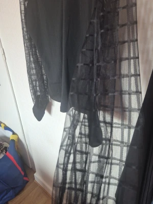 Svart meshblus med rutiga ärmar - Trendig svart blus från ChicMe med transparenta meshärmar i rutigt mönster. Blusen har en klassisk krage och långärmad design. Kroppen är i slät svart tyg medan ärmarna är i tunn mesh för en cool kontrast.