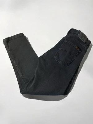 Mörkblå jeans från Nudie Jeans - Säljer ett par mörkblåa jeans från Nudie Jeans med klassisk femficksmodell och diskret logga på bakfickan. Jeansen har raka ben och är tillverkade i mjuk bomullsdenim med stretch för extra komfort. Perfekta för en clean och stilren look.