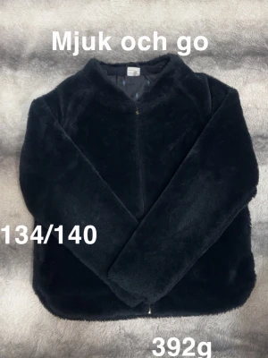 Svart pälsjacka i fuskpäls - Svart pälsjacka i supermjuk fuskpäls med lång ärm och enkel, stilren design. Jackan har dragkedja framtill och en rundad krage som ger en cozy vibe. Perfekt för kalla dagar när du vill vara både varm och snygg.🌸 Mjuk och go. Fint använt skick. Storlek 134/140
