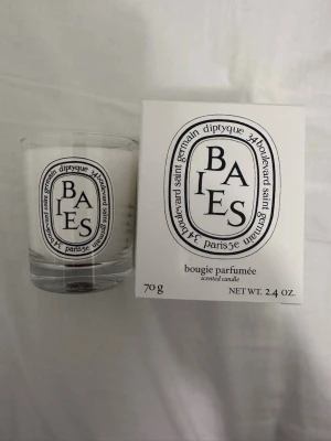 Diptyque Baies doftljus 70g - Säljer ett exklusivt Diptyque Baies doftljus på 70g. Ljuset kommer i en stilren glasbehållare med klassisk svartvit etikett och matchande förpackning. Perfekt för att skapa en lyxig känsla hemma med en fräsch och elegant doft.
