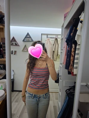 Randig croppad linnetopp - Säljer en croppad linnetopp med smala axelband och horisontella ränder i rött, vitt och svart. Toppen har en slim passform och är perfekt för varma dagar. Den har också dubbelt tyg framtill uppe som syns på bild 3. Enkel och stilren design som passar till jeans eller kjol.