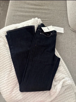 Mörkblå raka jeans från ONLY - Säljer ett par mörkblå jeans från ONLY med bootcut ben och klassisk femficksmodell. Jeansen har hög midja och detaljer i silver samt en brun logopatch bak i midjan. Materialet är kraftig denim som ger en snygg och tidlös look.