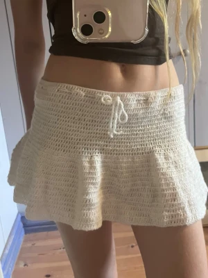 Vit virkad kjol - Säljer en vit virkade kjol med snörning i midjan. De har en utsvängd, form och är perfekta för sommaren. Materialet är luftigt och ger en avslappnad vibe.