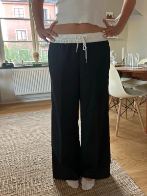 Svarta vida track pants - Säljer ett par svarta track pants med bred passform. Kan ha både lågmidjade och högt. 