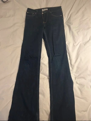 Mörkblå bootcut jeans  - Säljer ett par mörkblå bootcut jeans med klassiska fem fickor och kontrastsömmar. Jeansen har hög midja och utsvängda ben, perfekta för en retroinspirerad look. Materialet är kraftigt denim som ger en snygg siluett.