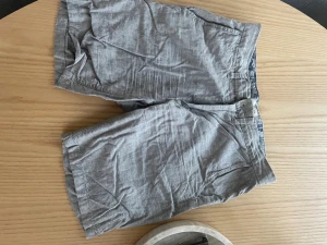 Gråa linne shorts  med fickor - Snygga grå shorts i linne med klassisk passform. Shortsen har sidofickor och bakfickor med knapp, perfekt för en avslappnad stil. Lätta och sköna för varma dagar.