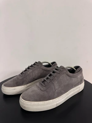 Grå Arigatos - Säljer dessa snygga sneakers från Axel Arigato. Skorna är i bra skick, men finns fortfarande täcken på användning.  Skorna är i en grå mocka, storlek 42. Hör av dig vid frågor! 