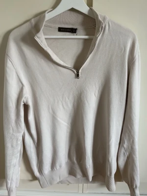 Beige halvzip-tröja från Oscar Jacobsson - Snygg beige tröja från Oscar Jacobsson  med halv dragkedja vid halsen. Tröjan har lång ärm, ribbade muddar och är tillverkad i ett mjukt material som känns skönt mot huden. Perfekt för lager-på-lager och enkel att matcha med jeans eller chinos. Orginalpris 1600