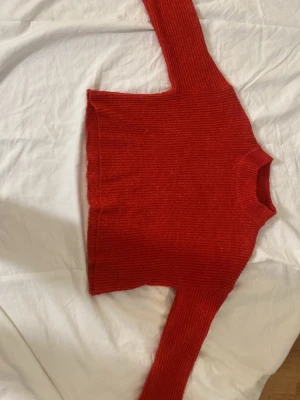 Röd ribbstickad tröja - Säljer en snygg röd ribbstickad tröja med vida ärmar nertill.Tröjan har en rak passform och är gjord i ett mjukt, stretchigt material som känns skönt mot huden. Perfekt till julen tillexempel 