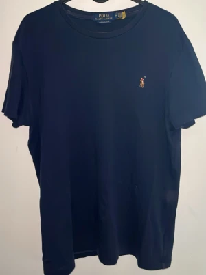 Mörkblå t-shirt från Polo Ralph Lauren - Mörkblå t-shirt från Polo Ralph Lauren i modellen Custom Slim Fit. Klassisk design med rund hals och liten broderad logga på bröstet. Perfekt för en clean och stilren look.