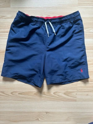 Marinblå badbyxor från Polo Ralph Lauren - Säljer ett par snygga marinblå badbyxor från Polo Ralph Lauren i storlek L. Jag har aldrig använt dem pågrund av att dem var för små för mig men hör gärna av dig vid frågor eller intresse :)