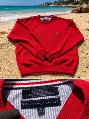 Röd stickad tröja Tommy Hilfiger XL - Röd stickad tröja från Tommy Hilfiger med rund halsringning och diskret logga på bröstet. Tröjan har ribbade muddar vid ärmslut och nederkant. Tillverkad i bomull och passar perfekt för en stilren och avslappnad look. Står xl men passar M skulle jag säg