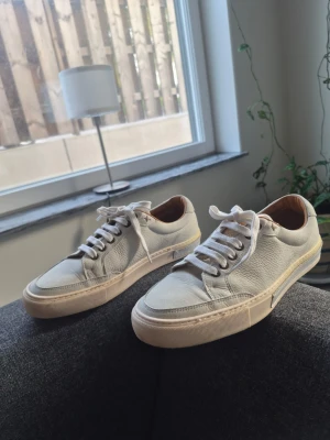 Sebago Sneakers i äkta läder mint grön färg Storlek 41 - Säljer ett par stilrena vita sneakers i läder med beige sula och vita skosnören. Skorna har en klassisk låg siluett och bruna detaljer på insidan. Perfekta för dig som gillar minimalistisk och clean stil.