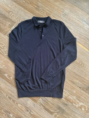 Mörkblå stickad tröja Dressmann - Mörkblå stickad tröja från Dressmann i merinoull. Tröjan har lång ärm, krage och tre knappar framtill. Perfekt för dig som gillar klassisk och stilren look med en mjuk känsla. Enkel att matcha med både jeans och chinos. Sista bilden är alltså hur den ser ut, tröjan finns ej längre i marinblå och är aldrig använd