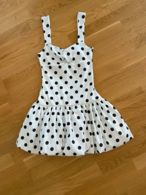  Ny slutsåld Vit kort klänning med svarta prickar ny med prislapp  - Supersöt vit kort klänning med breda axelband och svarta prickar. Klänningen har en markerad midja och voluminös kjol som ger en lekfull look. Perfekt för varma dagar och somriga vibes.