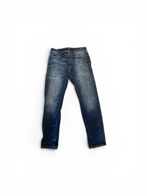 Blå jeans från Jack & Jones - Snygga blå jeans från Jack & Jones, modell Tapered/Mike. Jeansen har en klassisk femficksdesign, normalhög midja och avsmalnande ben. Materialet är denim i bomull  och tvättade detaljer för en cool look. Storlek W30 L 32