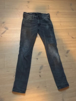 Replay jeans  - Säljer ett par grå slim fit jeans med slitna detaljer och klassisk femficksdesign. Jeansen har en smal passform och är tillverkade i stretchigt material för extra komfort. Perfekta för en avslappnad och trendig look.