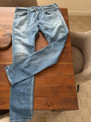 Blå jeans från Replay - Säljer ett par snygga blå jeans från Replay med klassisk femficksdesign och slitna detaljer. Jeansen har raka ben och är gjorda i mjukt denim-material. Perfekta för dig som gillar en avslappnad och trendig look.