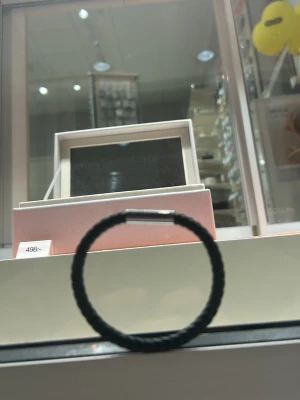 Svart flätat armband med metallås - Snyggt svart armband med flätad design och ett stilrent metallås. Armbandet har en enkel rund form och är gjort av textil eller läderliknande material. Perfekt för dig som gillar minimalistiska accessoarer.