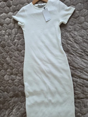 Vit ribbad klänning från Chiquelle - Snygg vit ribbad klänning från Chiquelle i storlek S. Klänningen har korta ärmar, rund halsringning och är figurnära i modellen. Tillverkad i ett stretchigt material som ger en bekväm passform. Perfekt för en stilren och trendig look.