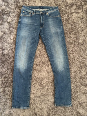 Blå slim fit jeans från Gant - Snygga blå slim fit jeans från Gant med klassisk femficksdesign och diskreta slitningar framtill. Jeansen har en Gant-logga på myntfickan. Perfekta för en avslappnad och trendig look. Storlek W34 L34