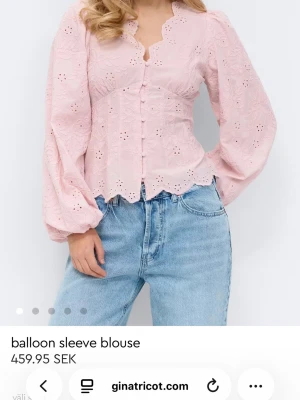 Ljusrosa blus med ballongärmar - Söt ljusrosa blus från Gina Tricot med broderade detaljer och ballongärmar. Blusen har knappar framtill, vågig kant nedtill och ett romantiskt hålmönster. Tillverkad i ett lätt tyg som ger en feminin och trendig look.