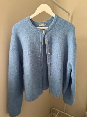 Ljusblå kofta från American Vintage - Mysig ljusblå kofta från Gina tricot med rund halsringning och knappar framtill. Koftan är stickad och har långa ärmar samt en avslappnad passform. Perfekt att slänga på sig när det är kyligt ute.