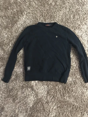 Svart sweatshirt med broderad logga - Svart sweatshirt med rund hals och lång ärm. Liten broderad logga på bröstet och en patch nertill. Klassisk och enkel design, perfekt till jeans eller joggers. Mjuk och bekväm bomullskänsla.