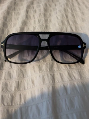  Tom Ford solglasögon - Snygga svarta/blåa solglasögon från Tom Ford med klassisk pilotbåge och mörka tonade glas. Ramen är i svart plast med guldiga T-detaljer vid gångjärnen. Perfekt accessoar för en cool look. Fick dubbla exemplar, därmed säljer jag dessa…😎