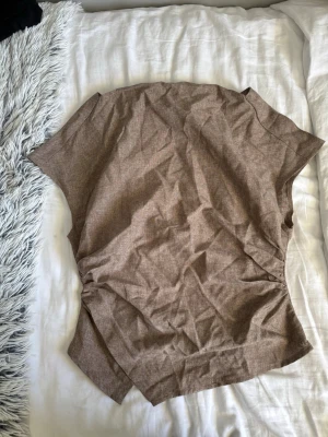 Brun kortärmad linnetopp - En brun kortärmad topp i linnematerial med enkel och avslappnad passform. Toppen har en rak form och är perfekt för en stilren och chill look. Passar till både jeans och kjol.