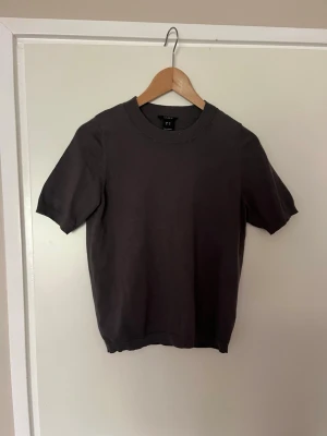 Grå stickad kortärmad topp - En stilren mörkgrå stickad topp med rund halsringning och korta ärmar. Toppen har en enkel och klassisk design som passar perfekt till jeans eller kjol. Materialet känns mjukt och bekvämt mot huden.