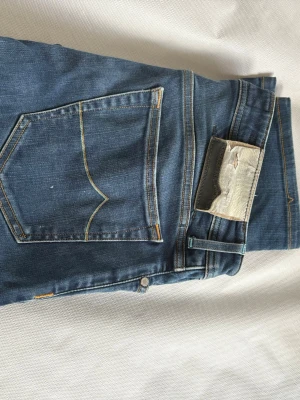 Blå jacob cohen jeans med klassisk passform - Säljer ett par blå jeans från jacob cohen med klassisk femficksmodell och tydliga kontrastsömmar. Jeansen har en rak passform och ikonisk läderpatch bak i midjan. Perfekta för en avslappnad och tidlös stil.