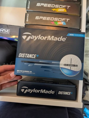TaylorMade Distance+ golfbollar - TaylorMade Distance+ golfbollar i vit färg, levereras i en blå och svart förpackning med tydlig logga. Bollarna har en plus alignment-linje för bättre riktning och är designade för extra längd. Perfekt för dig som vill ha mer distans på golfbanan.