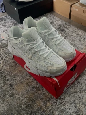 Nike p-6000 - Fräscha vita Nike sneakers med cool mesh- och skinnpaneler, chunky sula och snygga detaljer. Klassisk swoosh på sidan och extra vadderad plös för skön passform. Perfekta för dig som gillar stilrena och sportiga skor.