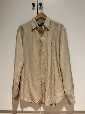 Beige linneskjorta från Ralph Lauren - Beige linneskjorta från Ralph Lauren i väldigt bra skick. Storlek medium men lite stor. Säljer då den är för stor för mig (183 cm)