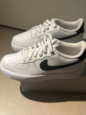 Nike Air Force 1 vita sneakers - Klassiska Nike Air Force 1 med svart swoosh i helt nytt skick och aldrig använda. Köpta för några år sedan men har endast förvarats. Originalkartong medföljer, dock något sliten