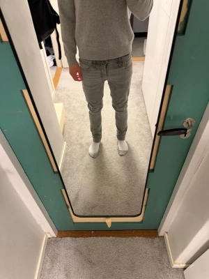 Grå slim fit jeans från Jack & Jones - Snygga grå slim fit jeans från Jack & Jones med klassisk femficksdesign och dragkedjegylf. Jeansen har en smal passform och är tillverkade i stretchigt denim för extra komfort. Perfekta för en stilren och modern look.