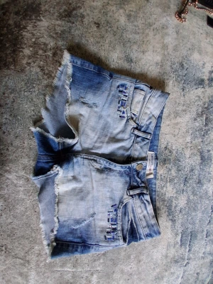 Blå denimshorts från Detroit - Snygga blå denimshorts från Detroit med slitna detaljer och fransig kant nedtill. Klassisk femficksmodell och normal passform. Perfekta för varma dagar och enkel att matcha med olika toppar.