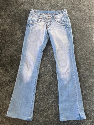 Ljusblå jeans med detaljer - Säljer ett par ljusblå jeans med dekorativa sömmar samt dragkedjor vid bakfickorna, de har även coola detaljer vid framfickorna. Jeansen har klassisk femficksmodell . Perfekta för en avslappnad och trendig look. Jeansen är i storlek 36 (men jämför gärna mått med ett par jeans du redan äger) ifrån märket Miss JoLie. Här är lite mått (mätt när jeansen ligger platt): Midjemått: ca 34cm, innerbenslängd: ca 78cm, grenmått: ca 18,5cm