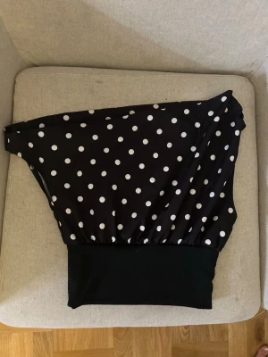 Svart prickig offshoulder topp från design by si - Cool svart offshoulder topp med vita prickar och ribbad mudd nedtill från designbysi. Materialet är mjukt, vilket gör den bekväm att bära hela dagen.