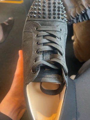 Svarta sneakers med nitar - Säljer ett par svarta sneakers med coola nitar på tån. Skorna har klassisk snörning och är tillverkade i ett matt material som ger en snygg och edgy look. Perfekt för dig som vill sticka ut och addera lite attityd till outfiten.