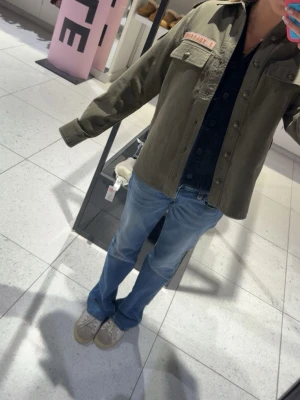 Grön jacka från Zadig & Voltaire - Stilren militärgrön overshirt från Zadig & Voltaire med två bröstfickor, axelklaffar och coola patchdetaljer. Jackan har knäppning framtill och en avslappnad passform som ger en trendig look. Aldrig använd så helt ny men utan prislapp, köpt för 3500kr!