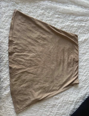 Beige A-linjeformad mockakjol - En enkel och stilren beige kjol i A-linjeform, tillverkad i mjuk mocka. Kjolen är kort och har en clean look utan detaljer eller mönster, perfekt för att matcha med olika toppar och sneakers.