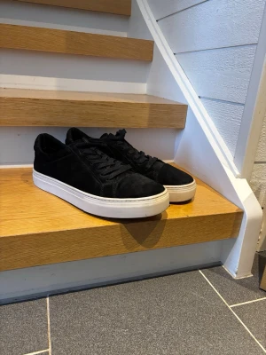Vagabond 2.0 Black - Snygga svarta sneakers med klassisk vit sula och svarta skosnören. Skorna har en låg profil och är tillverkade i mockaliknande material som ger en stilren och modern look. Perfekta för dig som vill ha en enkel men trendig sneaker.
