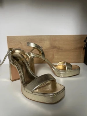 Guldiga balskor💛 - Säljer just nu dessa snygga guldiga blockheels i guld från Stradivarius. Skorna har en justerbar ankelrem och metallicfinish som ger en riktigt trendig look. Perfekta för för bal/sommar!! Köpta secondhand, endast provade av mig.🥰
