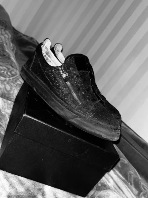 Svarta glittriga Giuseppe Zanotti - Säljer ett par svarta Giuseppe Zanotti med glitterdetaljer och dragkedja på sidan. Skorna har låg profil och klassisk rund tå. Materialet verkar vara syntet med glittrig finish. Perfekt för dig som vill sticka ut med en unik look. Använda två gånger studentdagen och på semester. Ny pris 7500kr