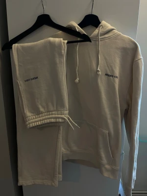 Beige hoodie och byxor från Axel Arigato - Säljer ett beige set från Axel Arigato med hoodie och mjukisbyxor. Hoodien har svart tryck 'ARIGATO ©2014' på bröstet och ryggen, stor ficka framtill och dragsko i huvan. Byxorna har elastisk midja och tryck på benet. Båda delar är gjorda i mjukt bomullstyg.