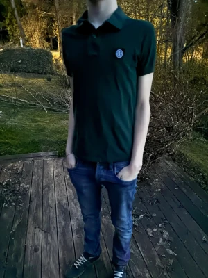 Mörkgrön Stone Island piké - Säljer en mörkgrön t-shirt från Stone Island med klassisk krage och korta ärmar. Modellen är 182 cm, hör av er vid funderingar
